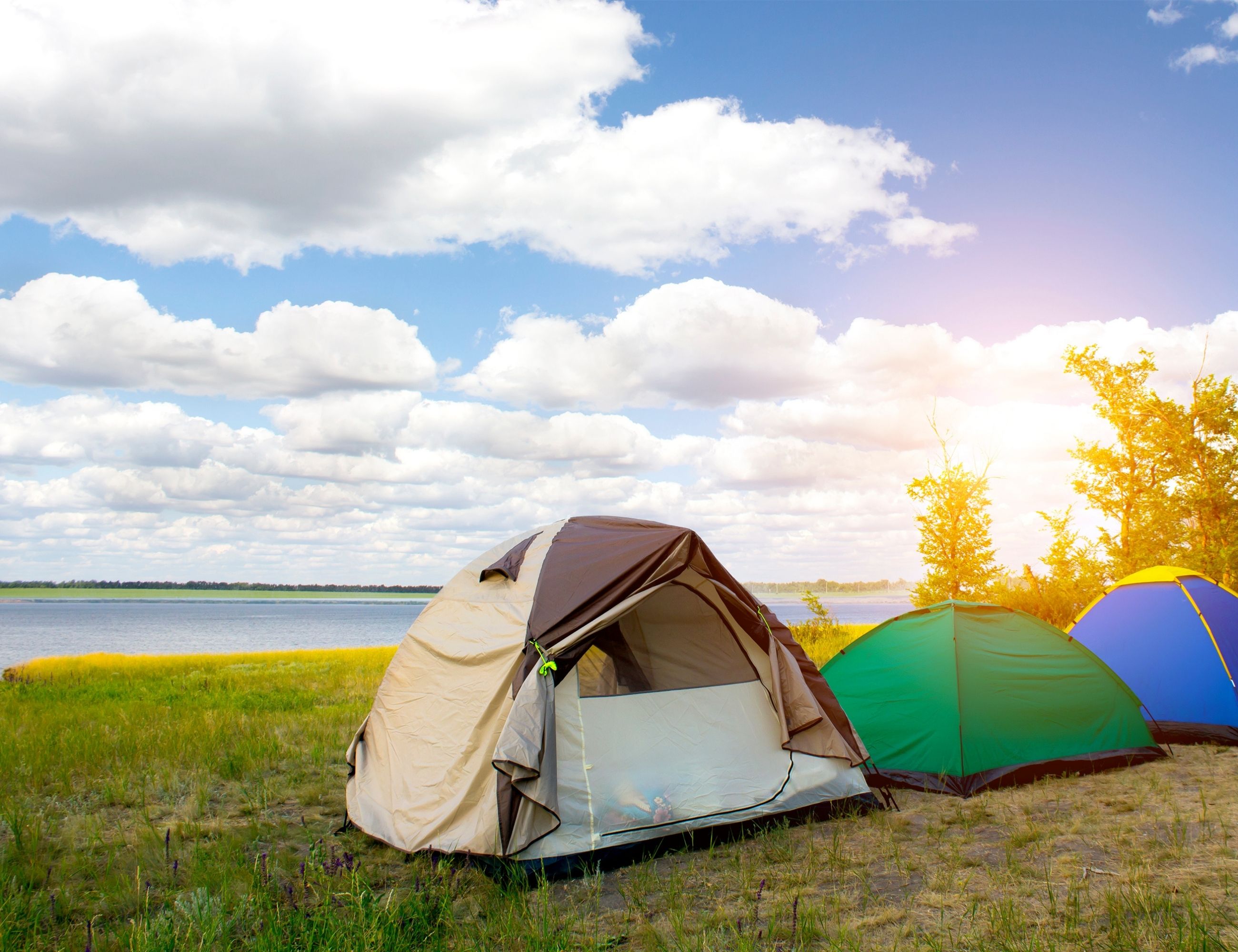 Image of three tents in front of a lake, blue sky with big fluffy clouds in the background